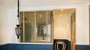 Ein Schlafzimmer mit einem Bett, einer Pendelleuchte, einem Fenster mit Jalousien, einem hölzernen Hocker und einem Kleiderschrank.