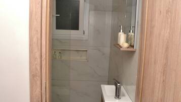 A bathroom with a glass shower enclosure, a white sink, and a mirror above the sink.