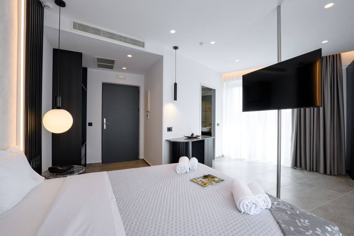 A modern hotel room with a large bed, a flat-screen TV, a desk with a chair, and a bathroom visible through an open door.
