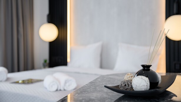 A neatly made bed with white linens and a black vase with decorative items on a marble table. - EcoHeaven Suites (Malevizi)