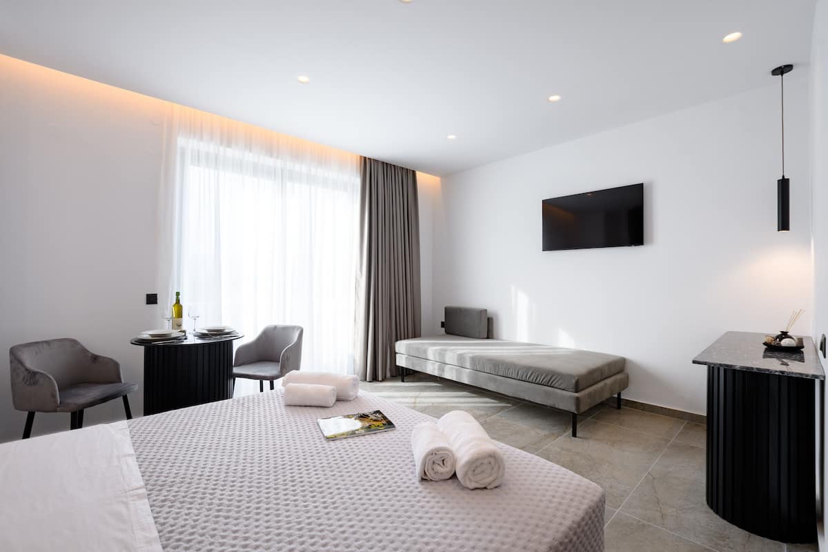 A modern hotel room with a bed, a desk, a chair, a TV, and a large window with curtains.