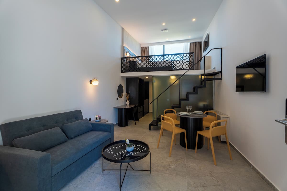 A modern living room with a sofa, coffee table, and dining area with chairs. A staircase leads to an upper level.