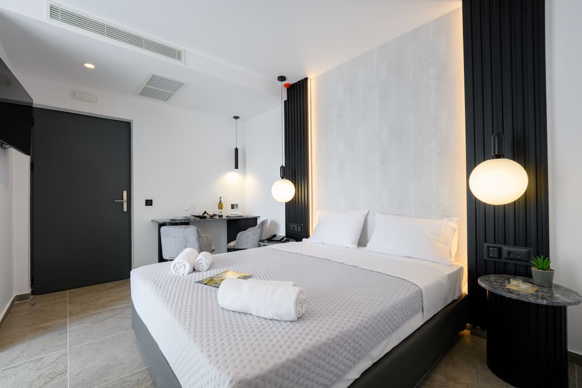A modern hotel room with a large bed, a desk, a chair, a small table with a plant, and a wall-mounted light fixture.