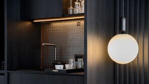 A modern kitchen with a black countertop, a sink, and a hanging light fixture. - EcoHeaven Suites (Malevizi)