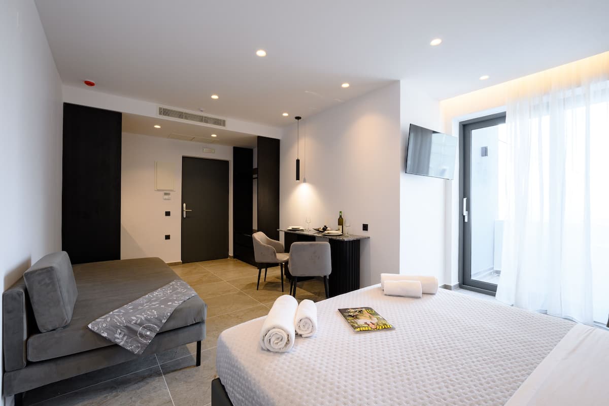 A modern hotel room with a bed, a sofa, a desk, and a television.