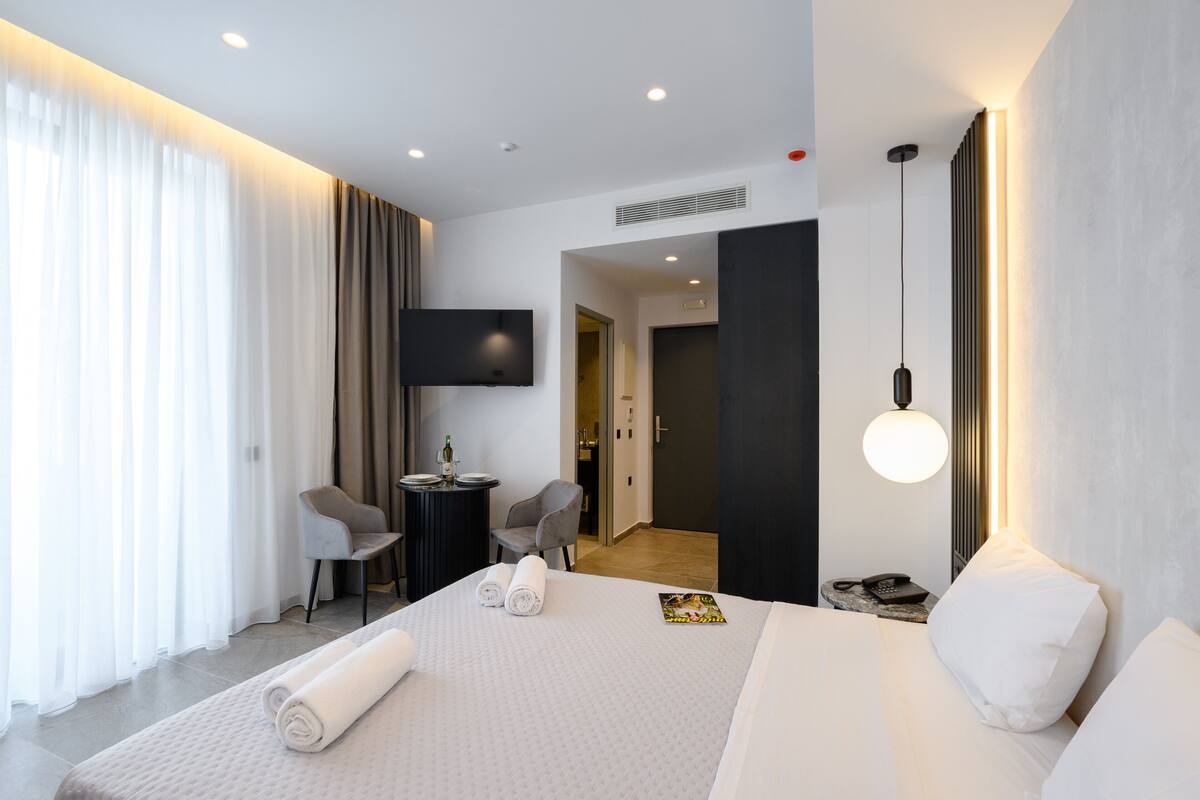 A modern hotel room with a large bed, a desk, a chair, and a TV on the wall.
