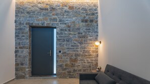 A modern living room with a stone wall, a dark door, a sofa, and a small table with a decorative item. - EcoHeaven Suites (Malevizi)