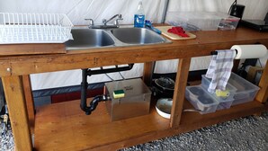 A kitchen with a wooden table, two sinks, a stove, and storage containers. - Glamping tent close to the river by Sundre, Alberta (James River Bridge)