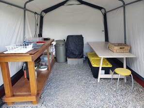 A tented area with a wooden table, a bench, a trash bin, and a table with a basket.