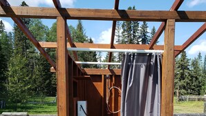 A wooden outdoor shower structure with a showerhead and a curtain. - Glamping tent close to the river by Sundre, Alberta (James River Bridge)