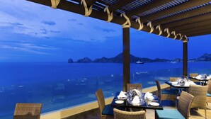 An outdoor dining area with tables and chairs, overlooking a body of water and distant landforms. - Villa del Arco  Beach Front. Grocery store on site or short ride. Full Kitchen.  (Cabo San Lucas)