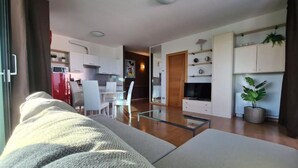 Ein modernes Wohnzimmer mit einem Glastisch, einer Couch und einem Essbereich mit weißen Stühlen.