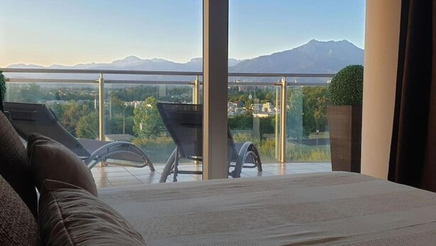 Ein Schlafzimmer mit einem großen Bett, Bergblick und einem Balkon mit Stühlen und einer Pflanze.
