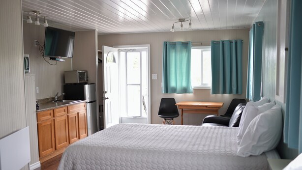 A bedroom with two beds, a kitchenette, a television, and a window with curtains. - Jackfish Lake Cottages Motel (Unorganized Thunder Bay District)
