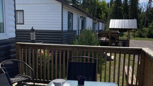 A wooden deck with a glass table, chairs, and a small table with a bowl and cups. - Jackfish Lake Cottages Motel (Unorganized Thunder Bay District)