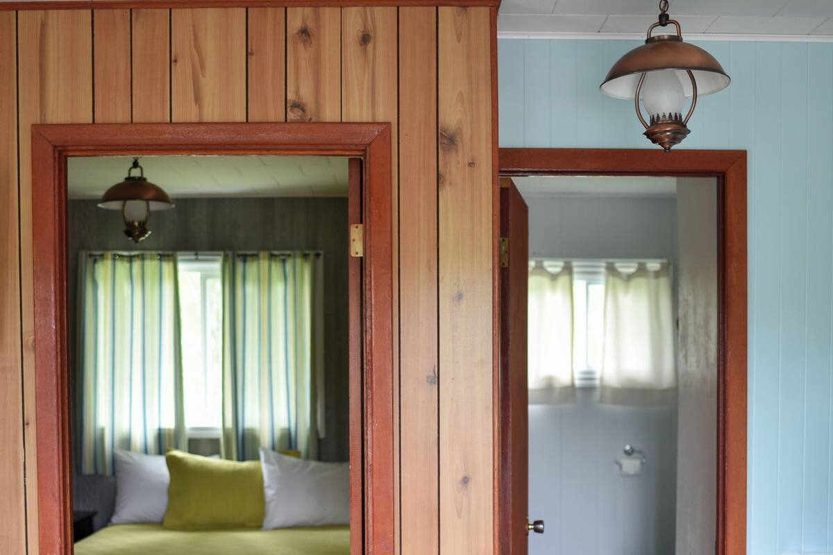 A room with a bed, a wooden table, and a bathroom visible through an open door.