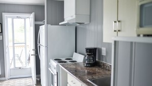 A kitchen with white cabinets, a stove, and a coffee maker. - Jackfish Lake Cottages Motel (Unorganized Thunder Bay District)