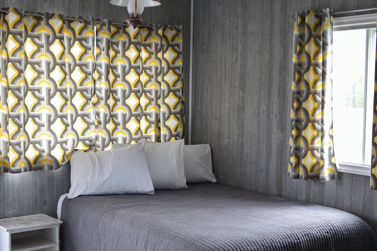 A bedroom with a bed, a nightstand, a patterned wall, and a window with curtains.