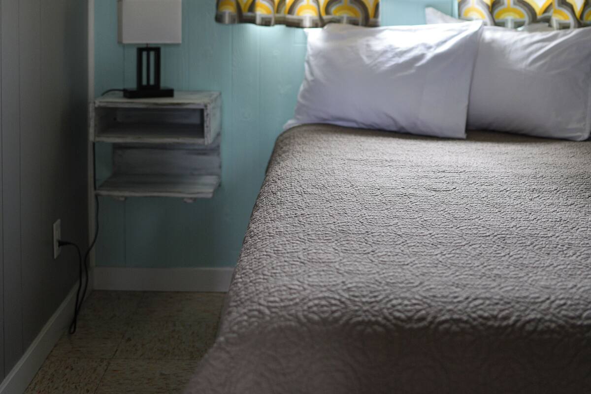 A bedroom with a bed, a nightstand with a lamp, and patterned curtains.