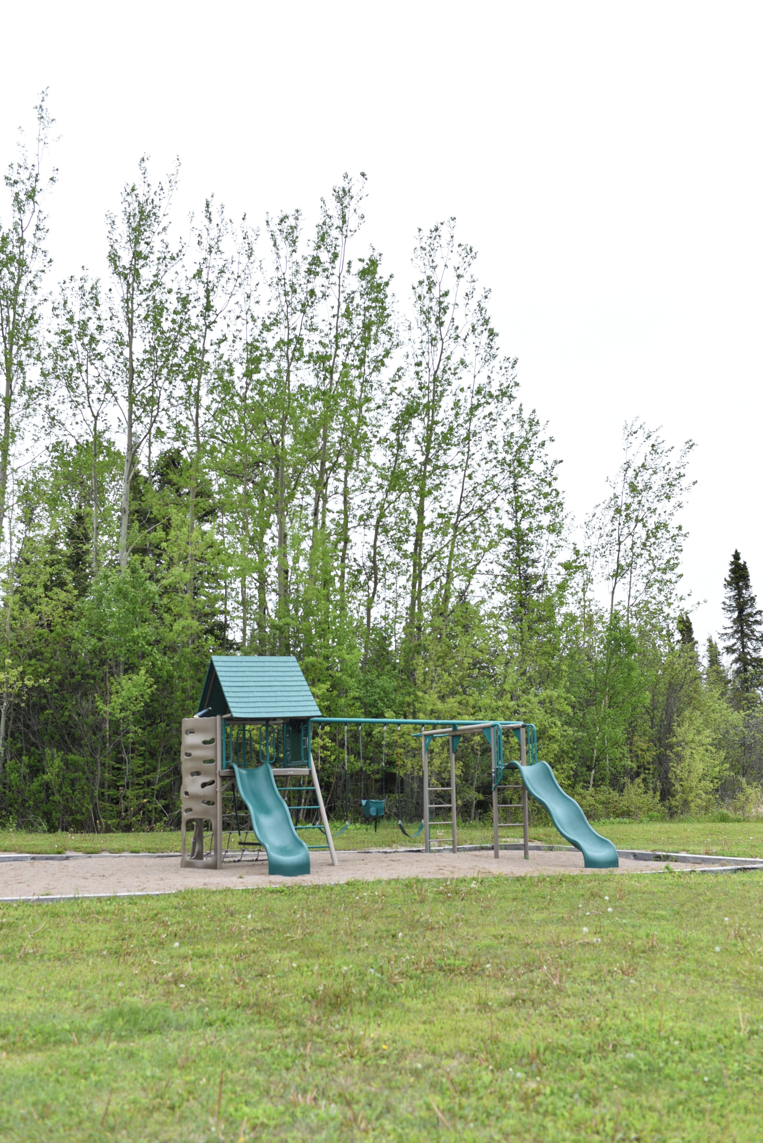 Un parc infantil amb tobogan i elements per escalar, envoltat d'arbres.