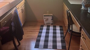Una cocina con ventana, armarios de madera, un tapete a cuadros y una caja de toallas de papel.