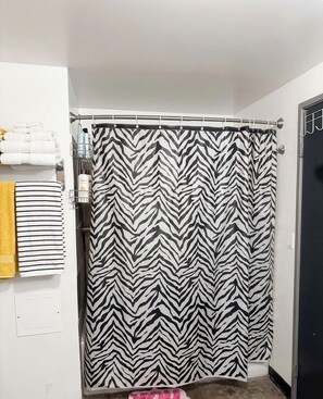 A bathroom with a zebra-striped shower curtain, a towel rack with folded towels, and a visible showerhead. - The Continental Royal Loft (Los Angeles)