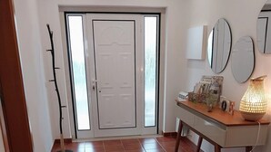 Un corridoio con un tappeto colorato, un pavimento in legno, una scrivania con una lampada e una porta con vetri satinati.