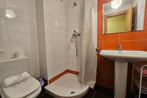 A bathroom with a shower, toilet, sink, and a mirror.