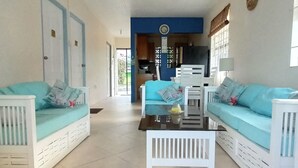 A spacious living area with two white sofas and a coffee table, a kitchen in the background, and a door leading outside. - Beachfront cottage with air conditioning and stunning views of Bathsheba  (Bathsheba)