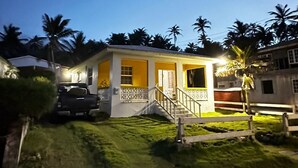 A two-story house with a yellow facade, a front porch, and a staircase leading to the entrance. - Beachfront cottage with air conditioning and stunning views of Bathsheba  (Bathsheba)