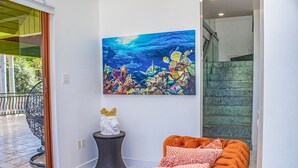 Un salon moderne agrémenté d’un grand tableau sur le thème de l’océan, d’un canapé orange moelleux et d’une petite table décorative surmontée d’une couronne dorée.