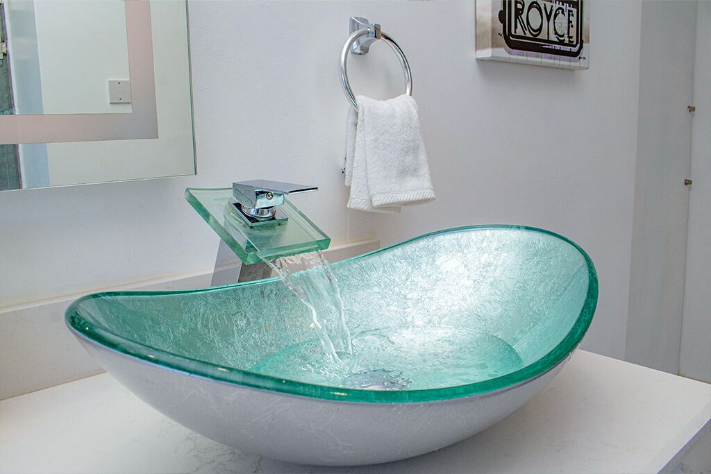 Un baño moderno con un lavabo de cristal, un perchero y un espejo.