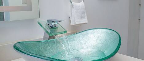 Un baño moderno con un lavabo de cristal, un perchero y un espejo.