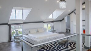 Une chambre à coucher moderne avec un grand lit, un tapis à motifs zébrés et une balustrade en verre donnant sur un balcon.