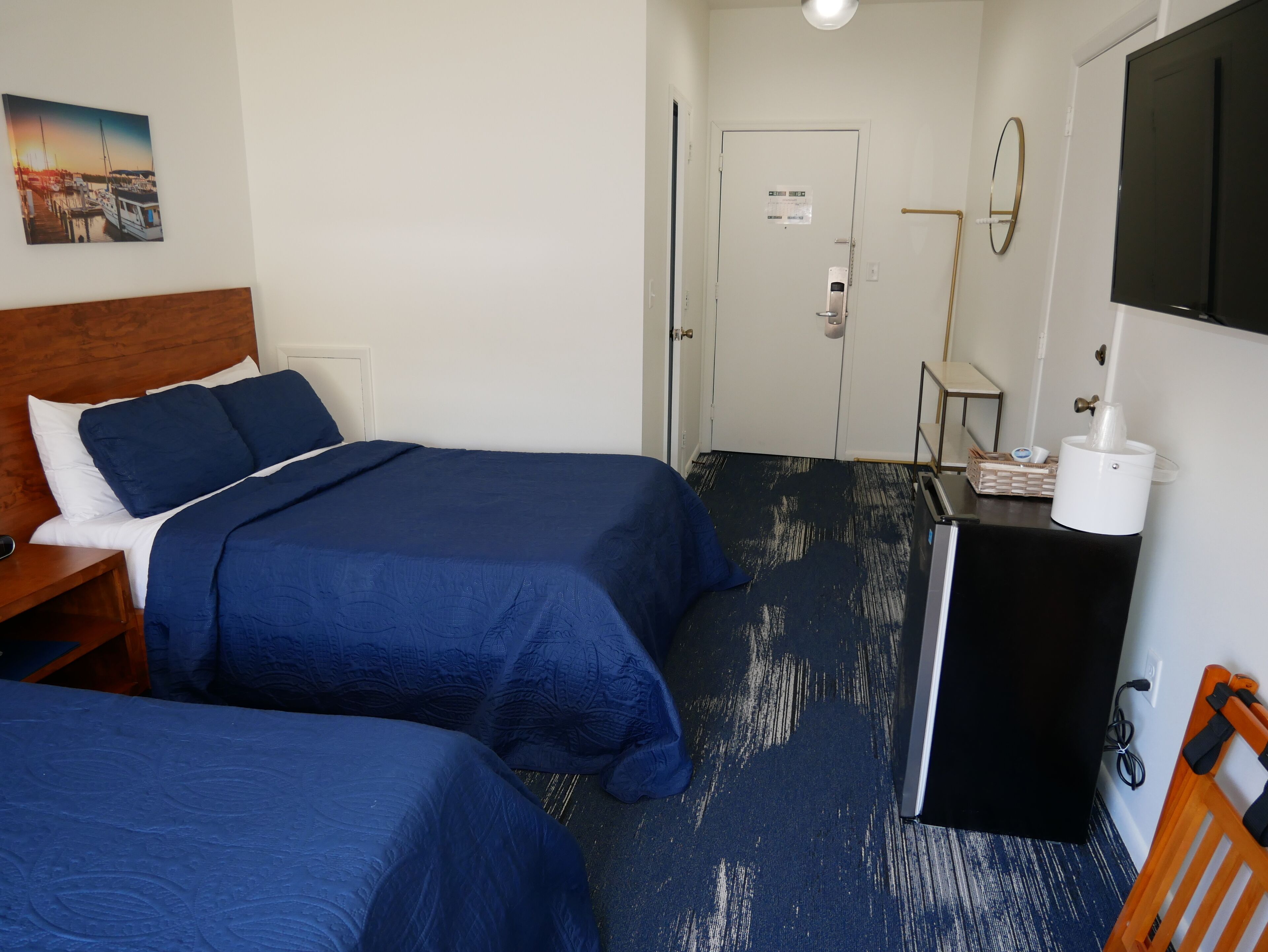 Ein Hotelzimmer mit zwei Betten, einem Schreibtisch, einem Sessel, einem kleinen Tisch mit Taschentuchhalter und einem Fernseher.