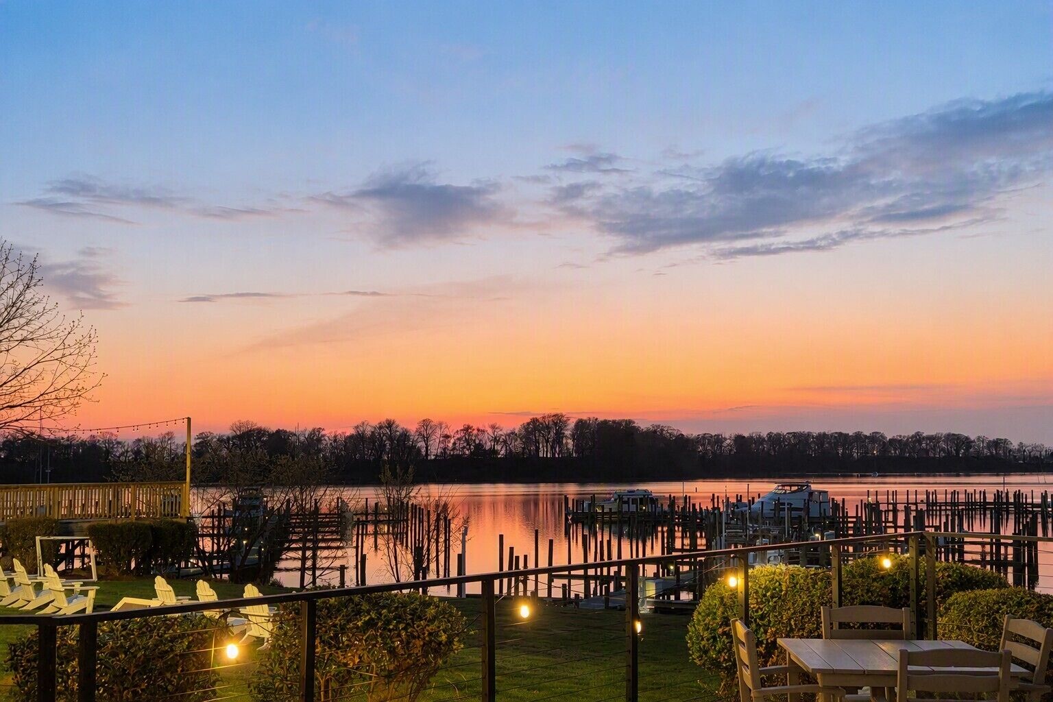 A lakeside view with a dock, chairs, and tables for outdoor dining.