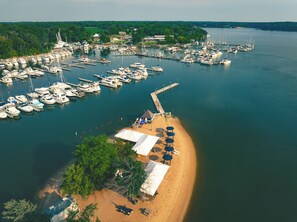 A marina with boats docked, a sandy beach with umbrellas, and a pier extending into the water. - The Lodge at Great Oak Landing (Chestertown)