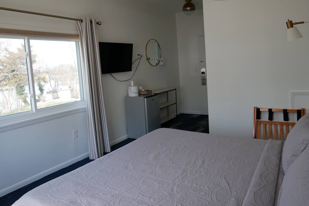 A bedroom with a bed, a desk, a TV, and a window with curtains.