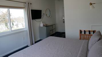 A bedroom with a bed, a desk, a TV, and a window with curtains.