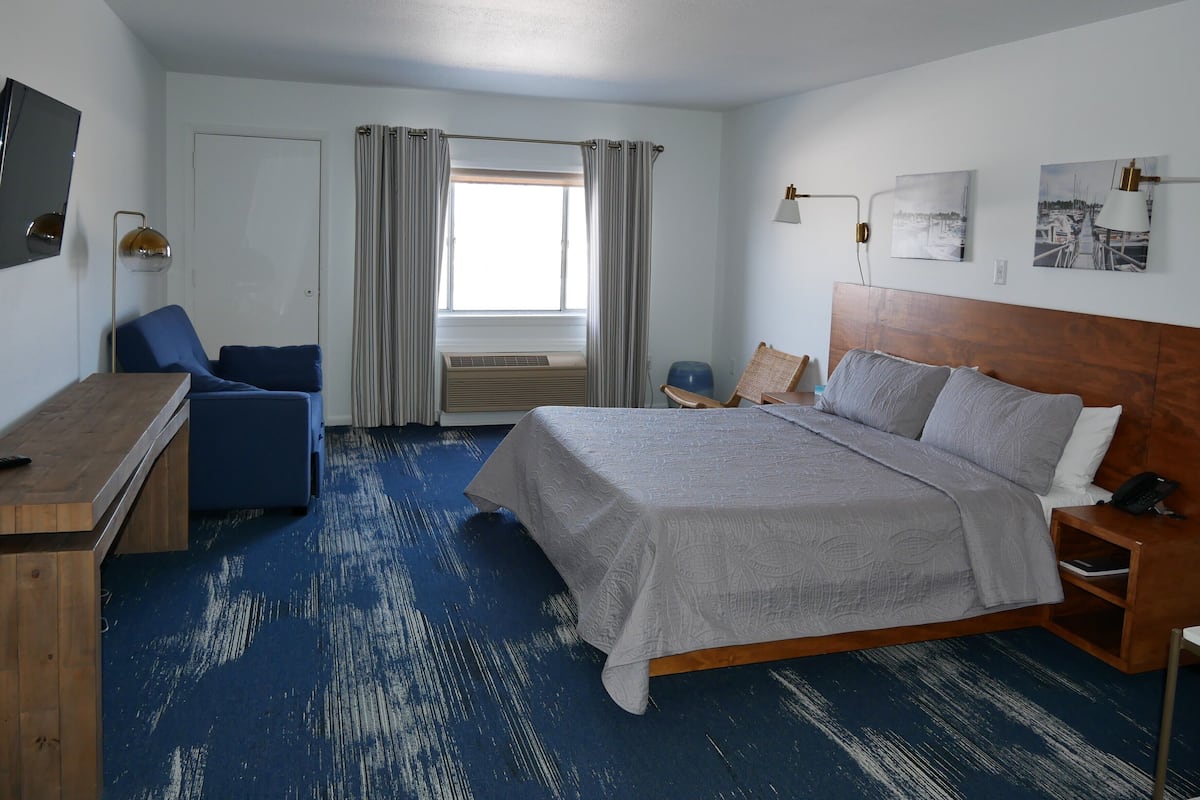 A hotel room with a bed, a desk, a chair, a window with curtains, and artwork on the walls.