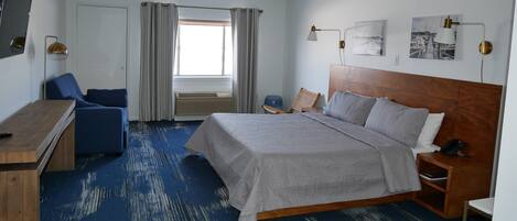 Une chambre d’hôtel comprenant un lit, un bureau, une chaise, une fenêtre avec des rideaux et des œuvres d’art accrochées aux murs.