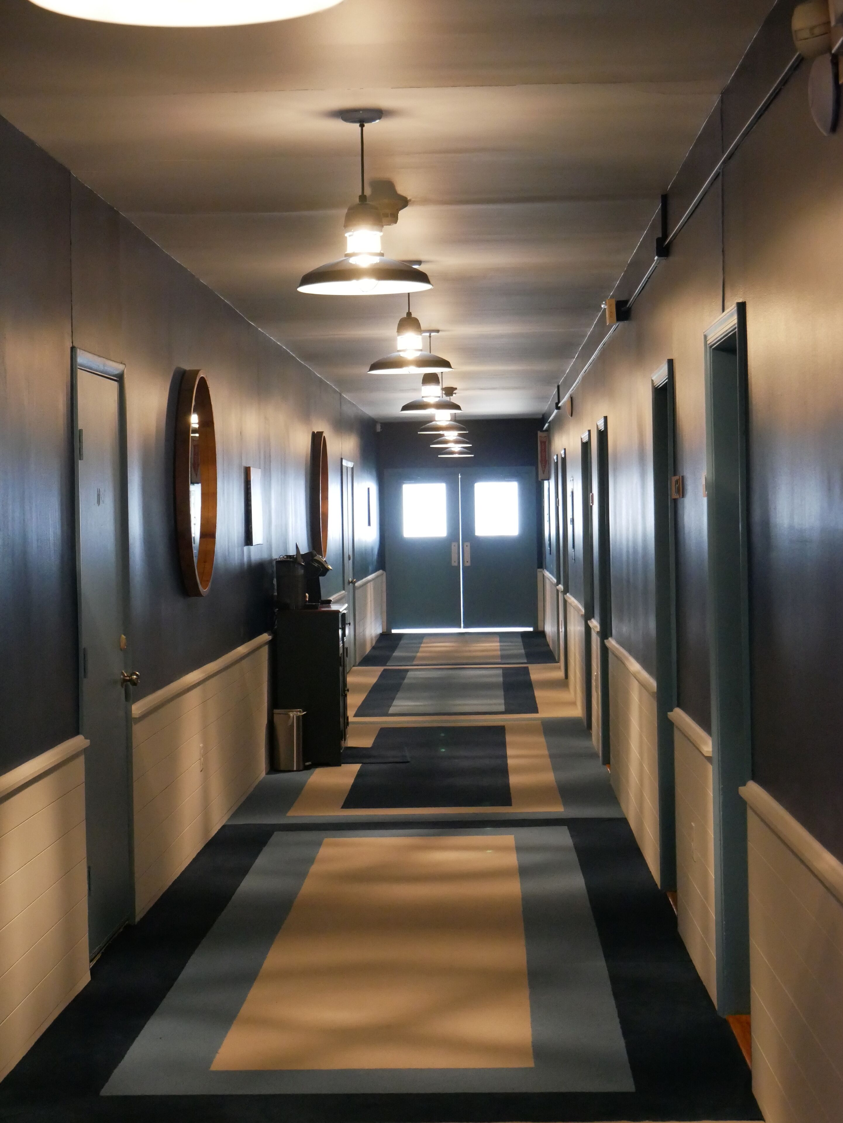A long hallway with a striped carpet, multiple doors, and pendant lights.