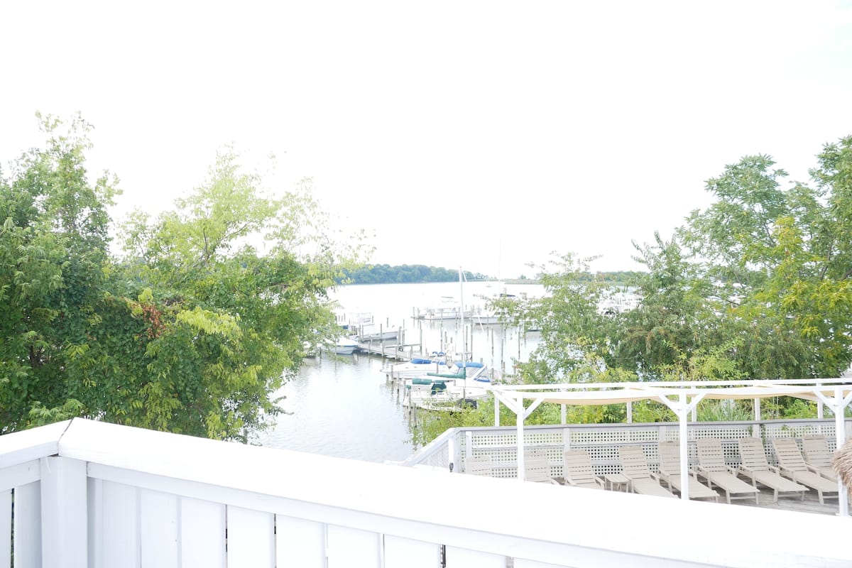 A marina with boats docked, surrounded by greenery and a white pergola with seating.