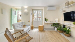 A modern living room with a white sofa, a wooden chair, a TV, and potted plants. - Perfect refuge in the city heart, 2 mins from the river, lakes and green spaces (Leiria)
