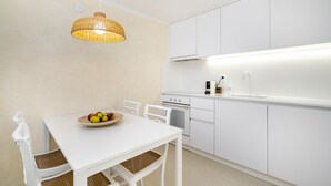 A modern kitchen with white cabinetry, a dining table with wicker chairs, and a wicker pendant light. - Perfect refuge in the city heart, 2 mins from the river, lakes and green spaces (Leiria)
