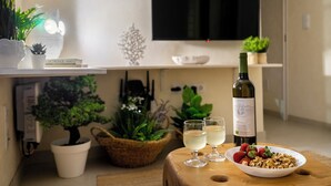 A modern living room with a flat-screen TV, a wine bottle, glasses, a bowl of strawberries and nuts, and various potted plants. - Perfect refuge in the city heart, 2 mins from the river, lakes and green spaces (Leiria)