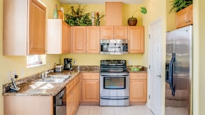Una cocina con armarios de madera, electrodomésticos de acero inoxidable y piso de baldosas.