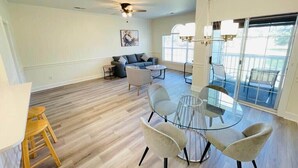 Un vaste espace de vie comprenant une table ronde en verre et des chaises, un canapé et un ventilateur de plafond.