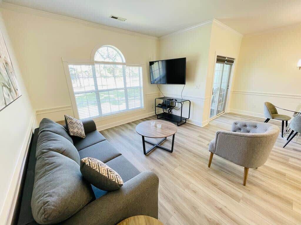 A living room with a sofa, armchair, coffee table, and a TV on a stand.