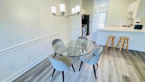Une cuisine moderne avec des meubles blancs, un réfrigérateur noir et une table à manger en verre, accompagnée de chaises.